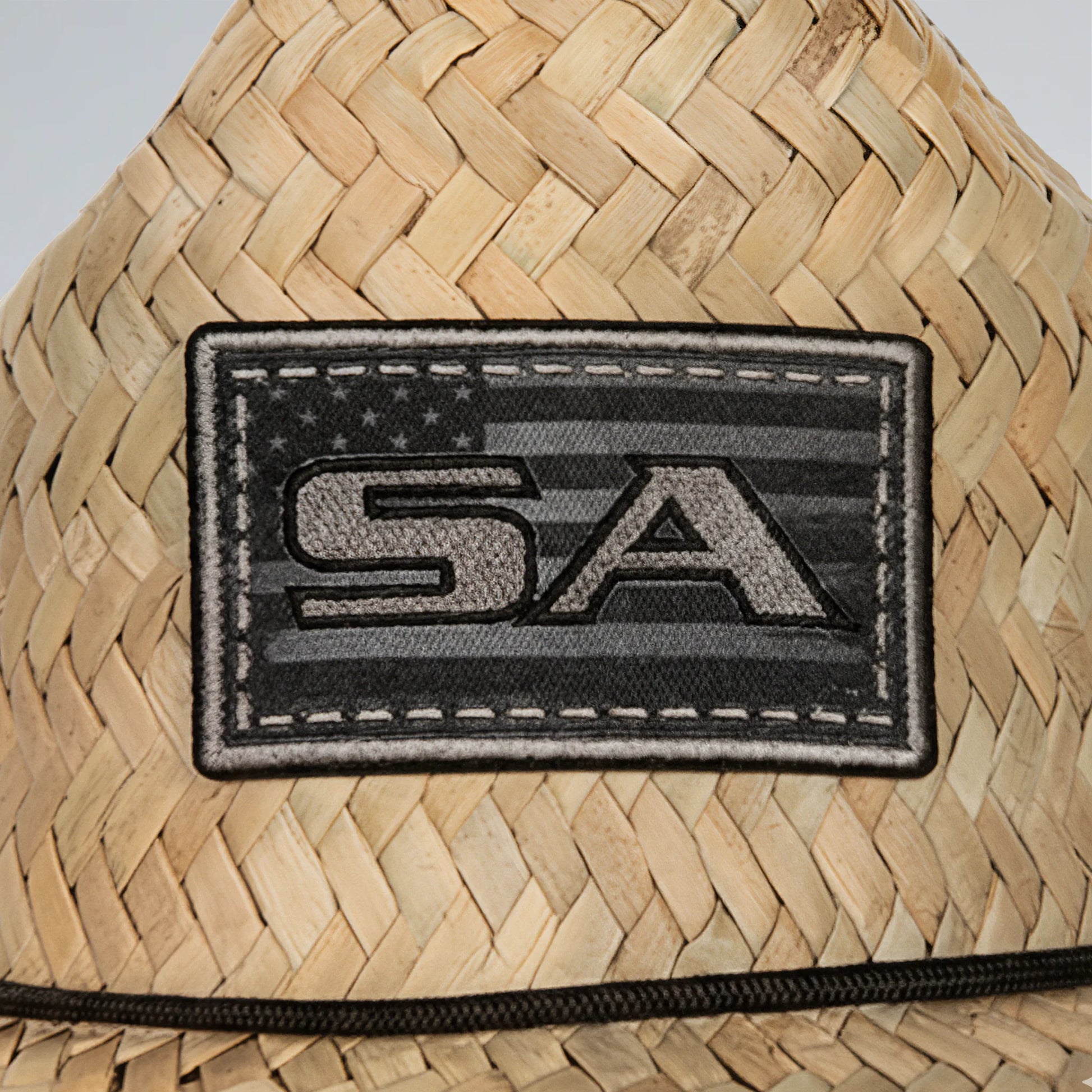 Woven straw hat with a black 'SA' patch on a neutral background