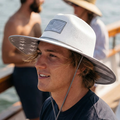 Man wearing a white sun hat with an American flag design, sitting on a boat.