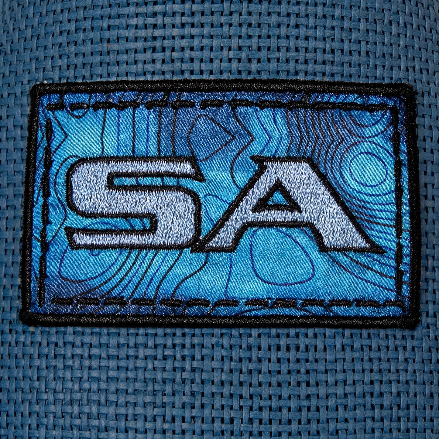 Embroidered patch with 'SA' initials on a textured blue fabric background