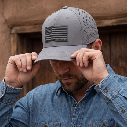 Man wearing a gray cap with an American flag patch, adjusting it against a wooden background.