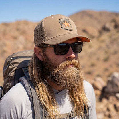 Man with a beard wearing sunglasses and a cap with a desert landscape in the background