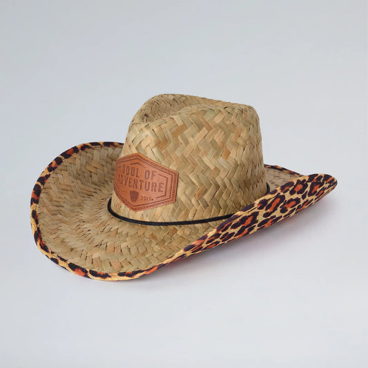 Straw cowboy hat with leopard print band and 'Soul of Adventure' patch on a light gray background