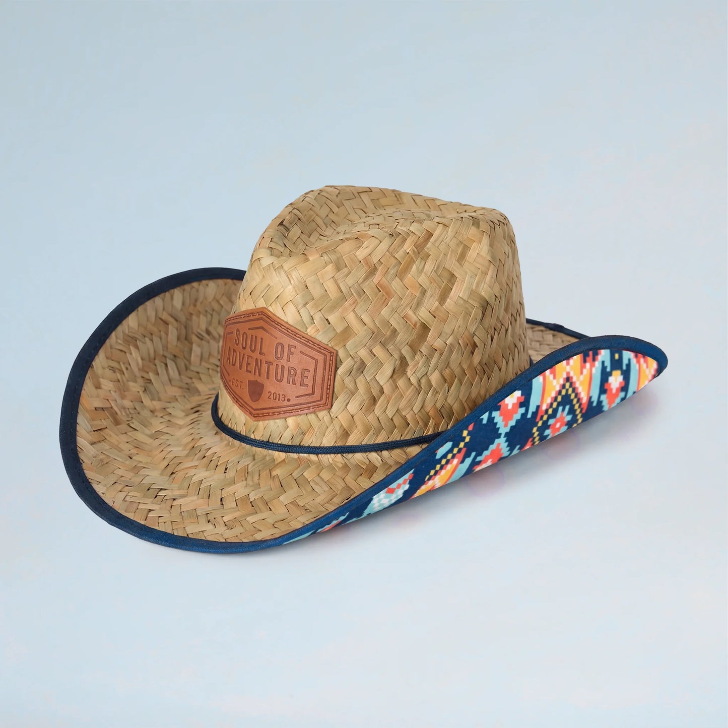 Straw cowboy hat with a colorful band and leather patch on a light blue background